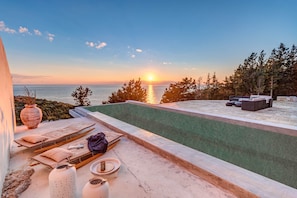 Piscina no terraço com espreguiçadeiras e vista para o pôr do sol sobre o mar.