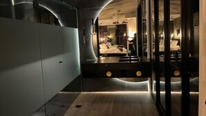 Une chambre d’hôtel moderne dotée d’un plafond incurvé, d’un grand lit, d’une table de chevet et d’un miroir qui reflète la pièce.