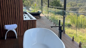 Une salle de bain moderne en plein air, dotée d’une grande baignoire blanche, d’un petit tabouret blanc et d’un jacuzzi.
