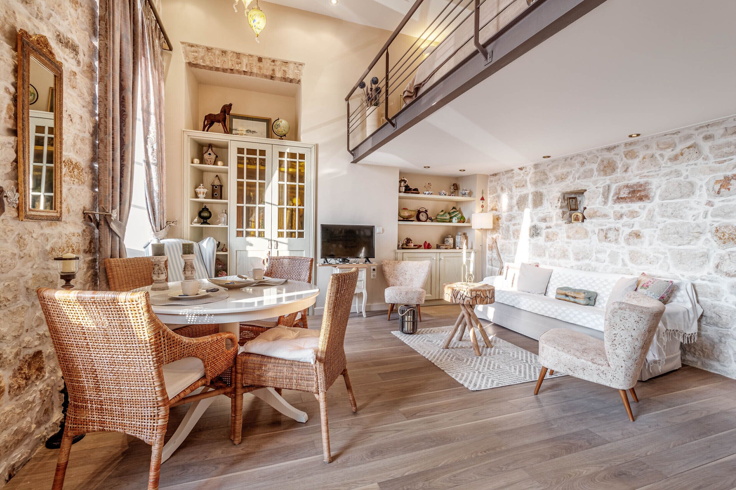 A spacious living area with a dining table, wicker chairs, a white sofa, and a stone wall.