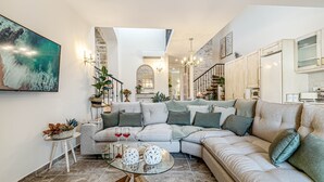 A modern living room with a sectional sofa, a glass coffee table, and a large abstract painting. - The Heritage Cottage in Doukades (Palaiokastritsa)