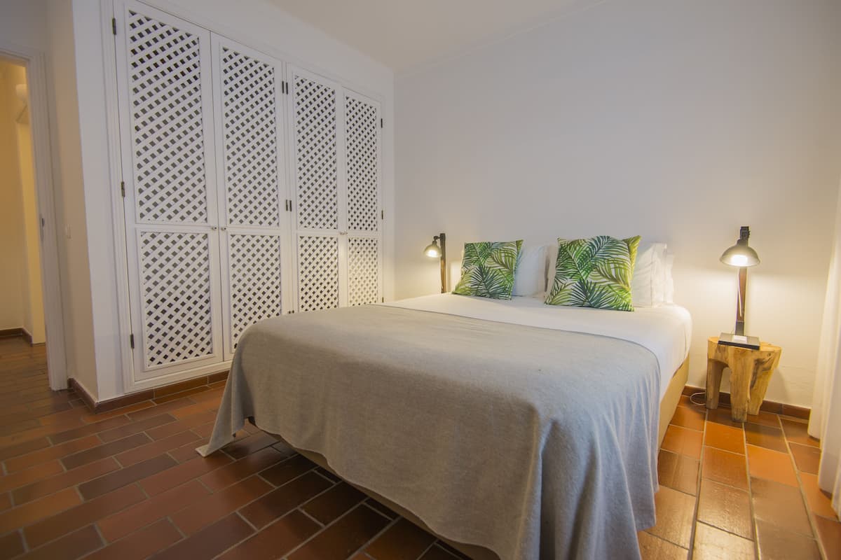 Une chambre à coucher avec un lit, deux lampes de chevet, une table de chevet en bois et une armoire blanche à persiennes.