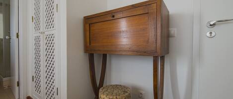 Um armário de madeira com uma gaveta, fixado numa parede com uma porta branca e um pequeno banquinho com base redonda.