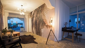 Une pièce avec un sol en pierre, un grand mur décoré de feuilles de palmier, un trépied et un bureau avec une lampe.