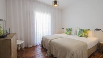 Ein Schlafzimmer mit zwei Betten, weißen Vorhängen, einer Pendelleuchte und einem kleinen weißen Stuhl.