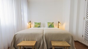 Un lit double avec deux oreillers, deux tables de chevet et deux lampes fixées au mur.