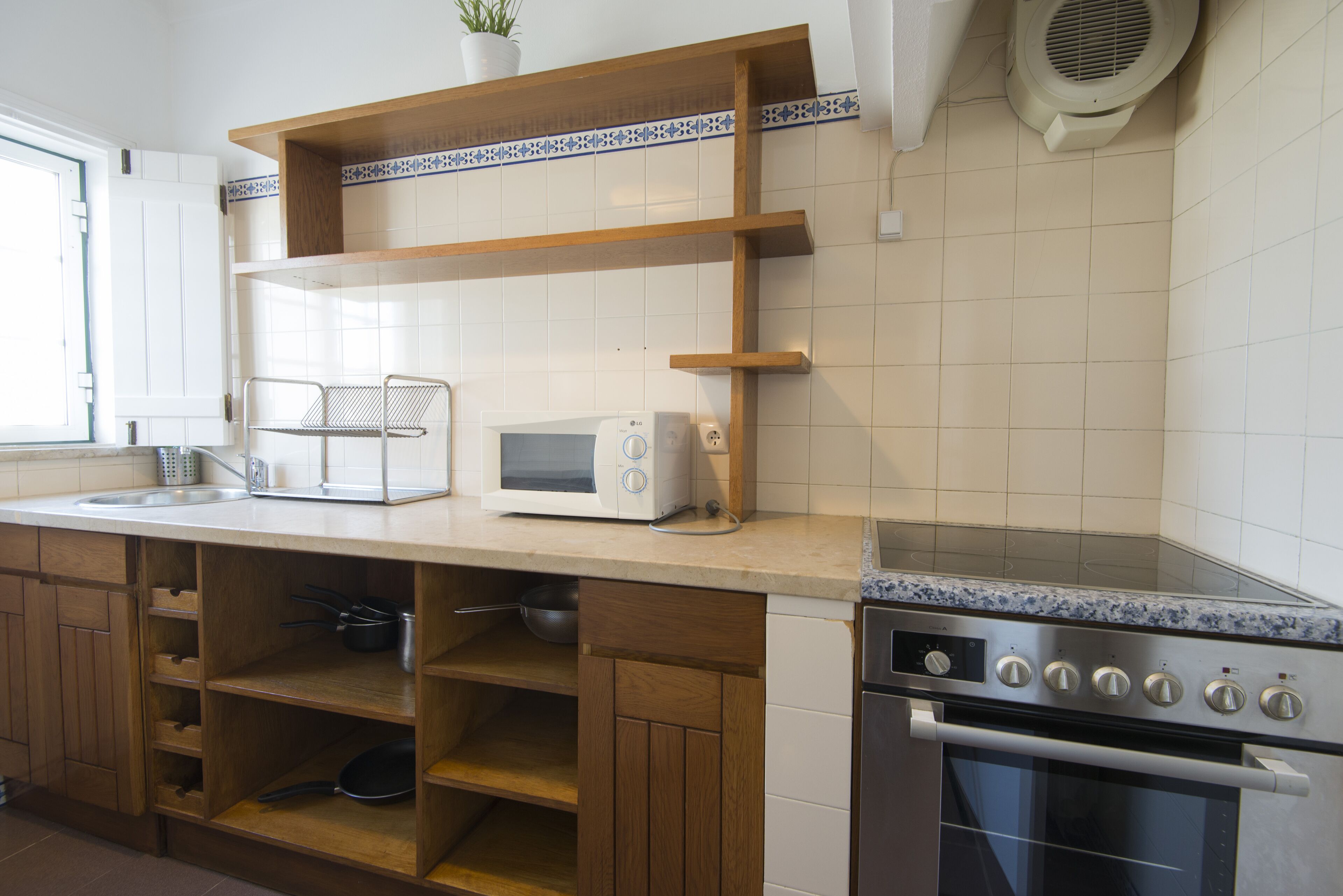 A kitchen with a microwave, stove, wooden shelves, and a potted plant.