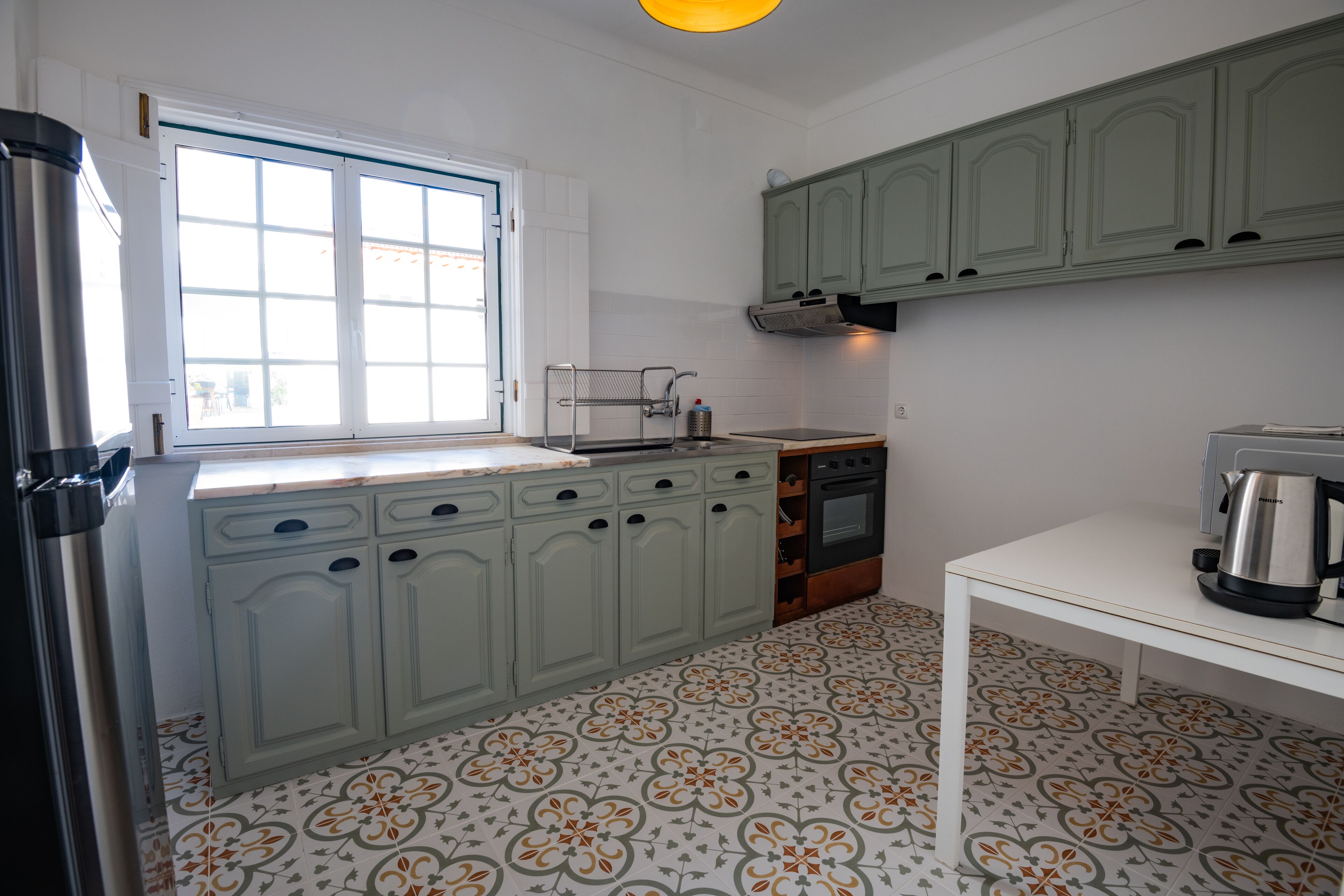 A kitchen with a window, white cabinets, a stove, and a coffee maker.