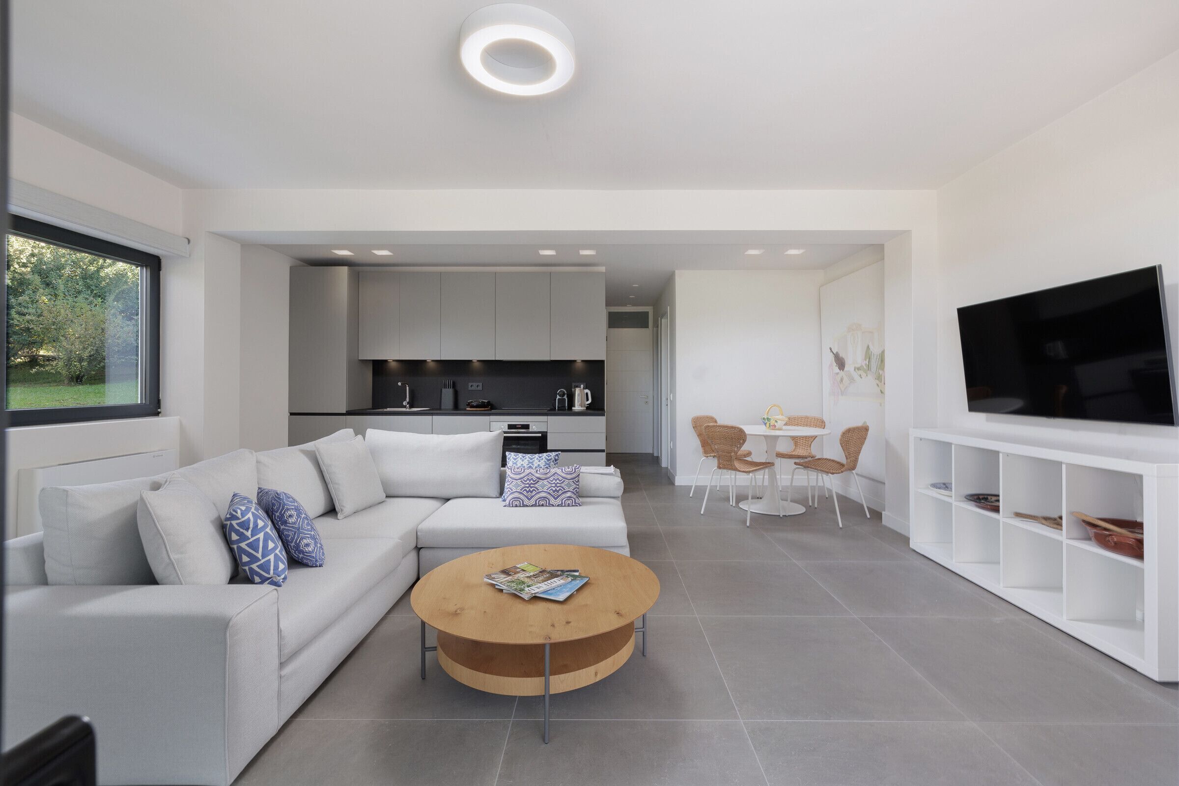A modern living room with a sofa, coffee table, TV, and kitchen in the background.