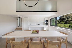 A modern kitchen with white cabinets, a large island, and a view of greenery outside.