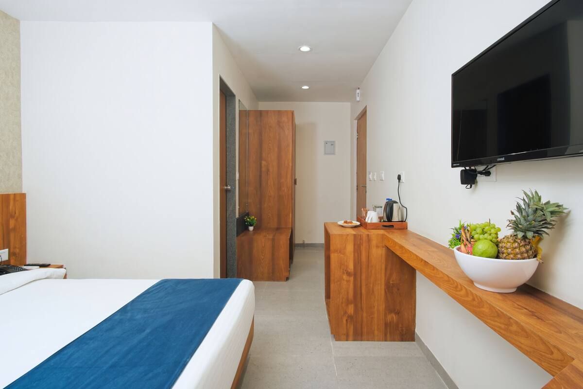 Una habitación de hotel con una cama, un escritorio de madera, un televisor montado en la pared y un frutero sobre el escritorio.