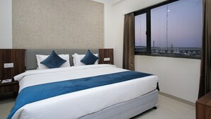 A hotel room with a large bed, a view of the cityscape, and a window with curtains. - Rishivan Hotels and Wellness (Dasada)