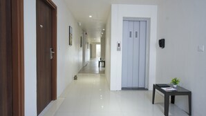 A hallway with wooden doors, a white wall, and a small table with a plant. - Rishivan Hotels and Wellness (Dasada)