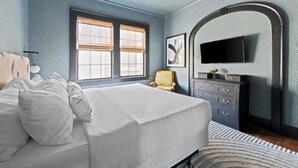 Een slaapkamer met een groot bed, een dressoir, een stoel en een televisie die aan de muur is bevestigd.