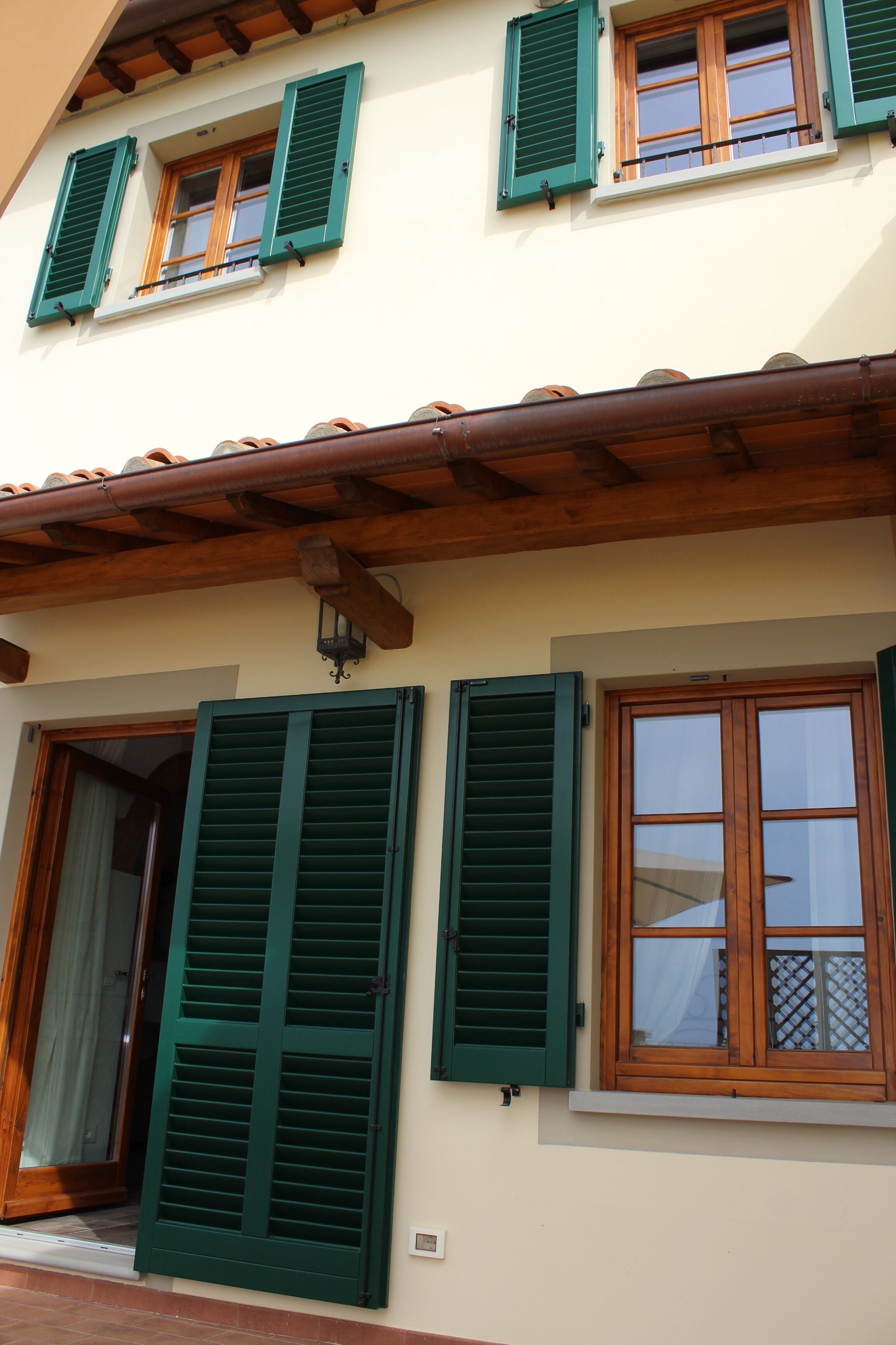 Ein Gebäude mit mehreren Fenstern, einige davon mit grünen Fensterläden, und einem Holzdach.