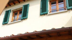 Un edificio con diverse finestre, alcune dotate di persiane verdi, e un tetto in legno.