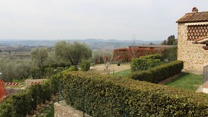 Un edificio in pietra con tetto in tegole, circondato da siepi curate e con vista su dolci colline.