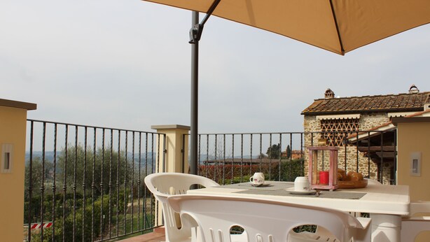 Un balcone con tavolo e sedie, vista sulla campagna e un edificio in pietra sullo sfondo.