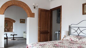 Una camera da letto con una coperta a fiori, una porta in legno, un arco in mattoni, un piccolo tavolo con una lampada e un quadro appeso al muro.