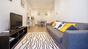 Ein modernes Wohnzimmer mit grauem Sofa, einem Flachbildfernseher, einem Couchtisch und einem gemusterten Teppich.