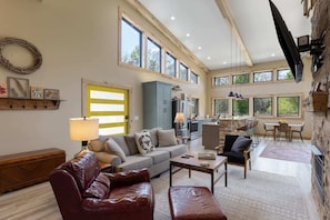 A spacious living area with a sofa, a coffee table, and a dining table. There is a kitchen area with a stone wall and a TV mounted on the wall.
