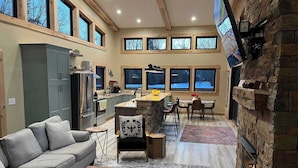 Una cocina amplia con una isla central, un comedor con chimenea de piedra y una sala de estar con sofá y mesa de centro.