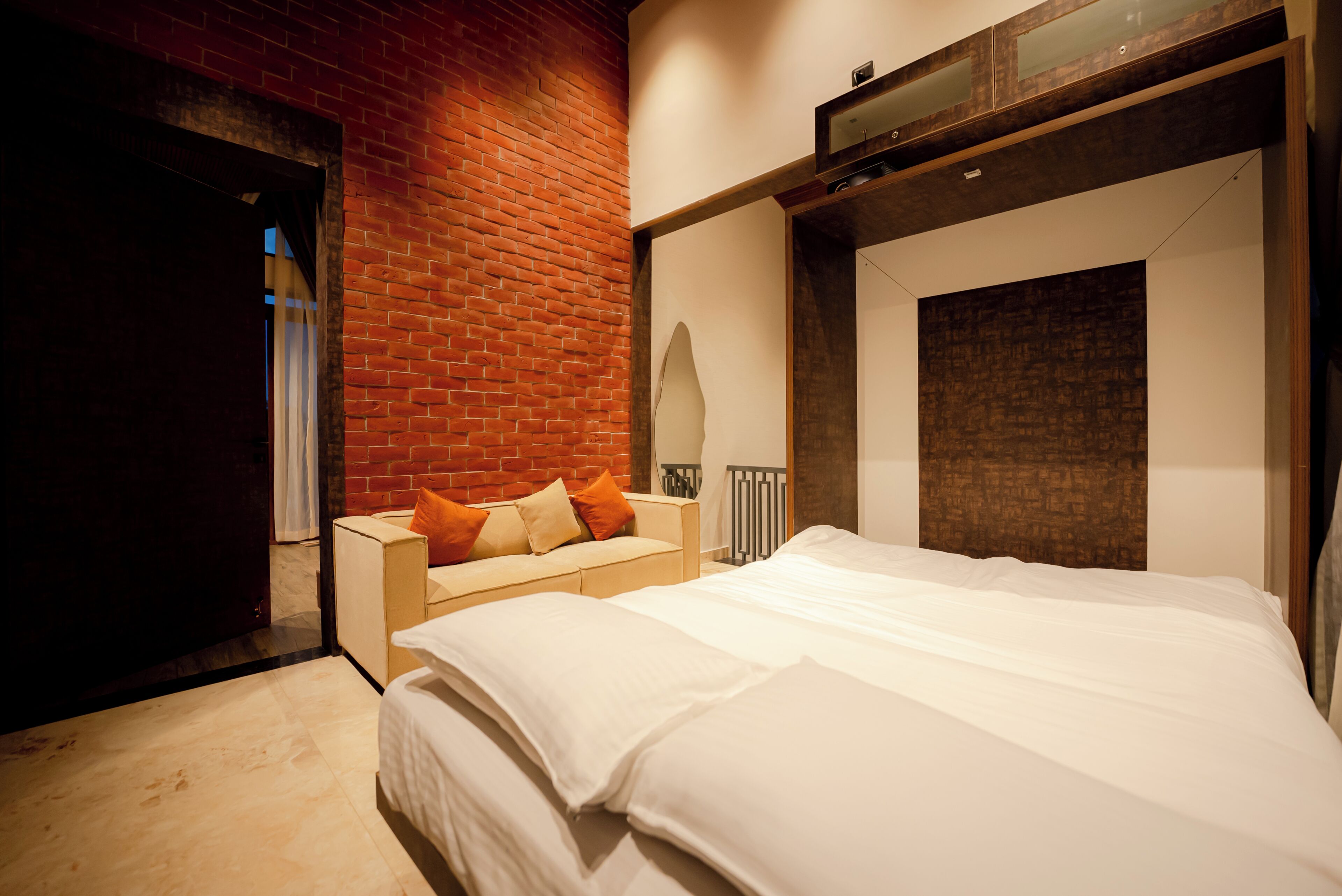 A bedroom with a brick wall, a bed with white bedding, a nightstand, and a wooden headboard.