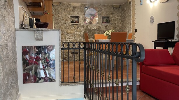 Un salon avec un mur en pierre, un canapé rouge, un téléviseur et un balcon doté d’une balustrade.