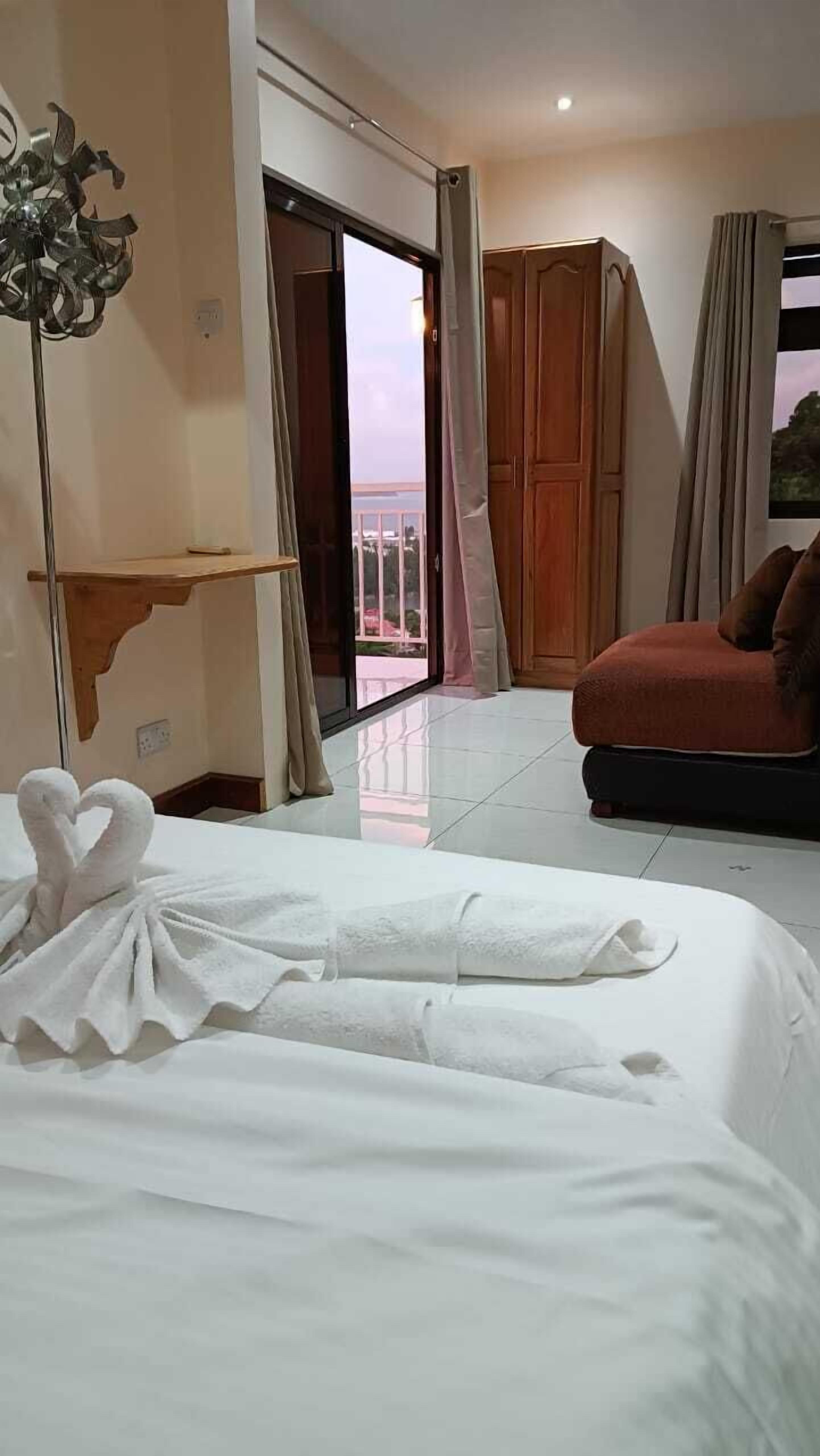A hotel room with a bed, a sofa, a wooden wardrobe, a balcony, and a decorative plant.