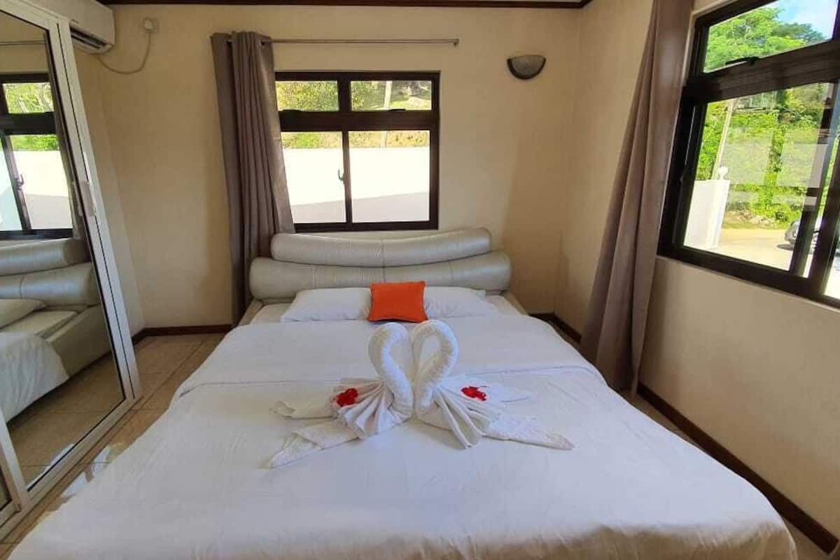 A hotel room with a bed, a sofa, a large window, and a mirror.