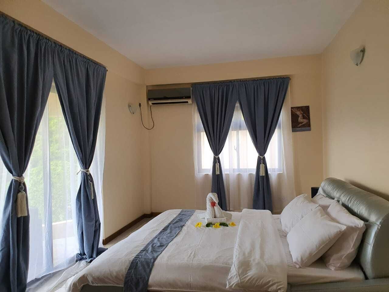 A hotel room with a bed, curtains, an air conditioning unit, and a wall-mounted light fixture.