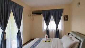 A hotel room with a bed, curtains, an air conditioning unit, and a wall-mounted light fixture.