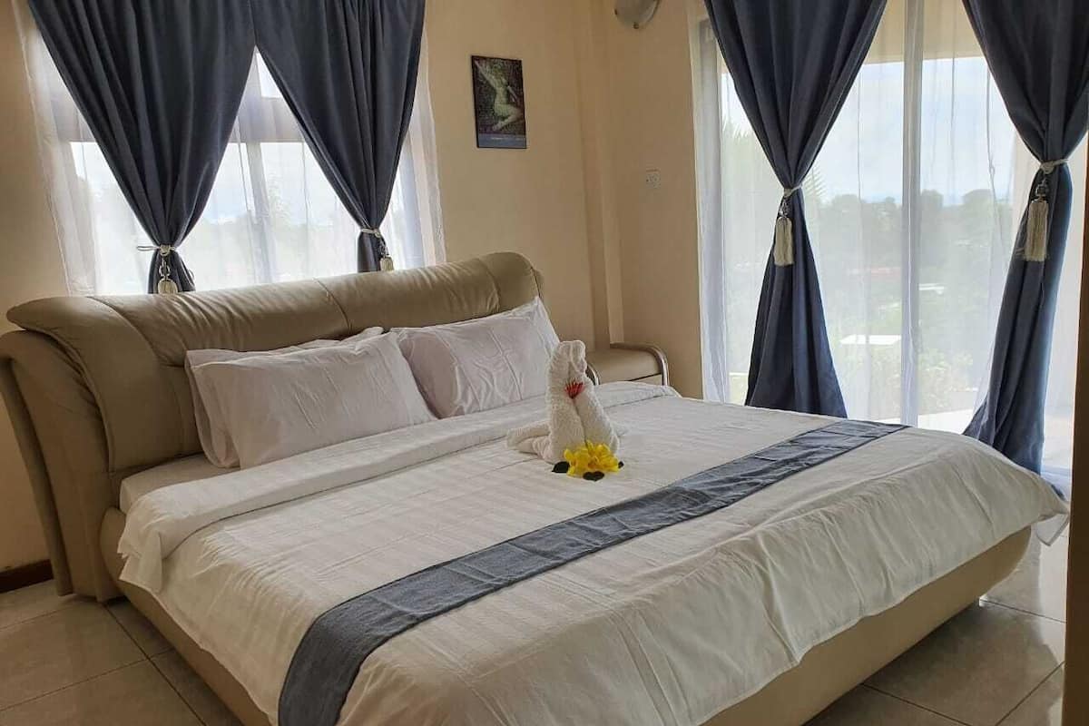 A large bed with a beige headboard and white bedding, curtains, and a small decorative item on the bed.