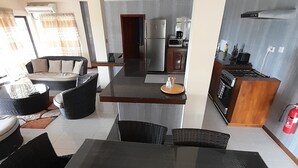 Ein modernes Wohnzimmer mit Esstisch und Stühlen, einer Couch und einer Küchenzeile mit Kühlschrank und Herd.
