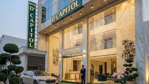 A hotel entrance with a sign reading 'D'CAPITOL,' a valet service, and a security guard. - Hotel D'Capitol- Delhi Airport (New Delhi)