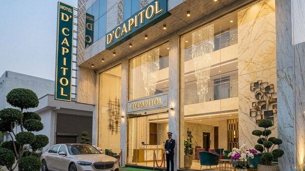 A hotel entrance with a sign reading 'D'CAPITOL,' a valet service, and a security guard. - Hotel D'Capitol- Delhi Airport (New Delhi)