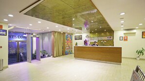 A hotel reception area with a wooden reception desk, a glass door entrance, and a ceiling with recessed lighting. - Hotel D'Capitol- Delhi Airport (New Delhi)