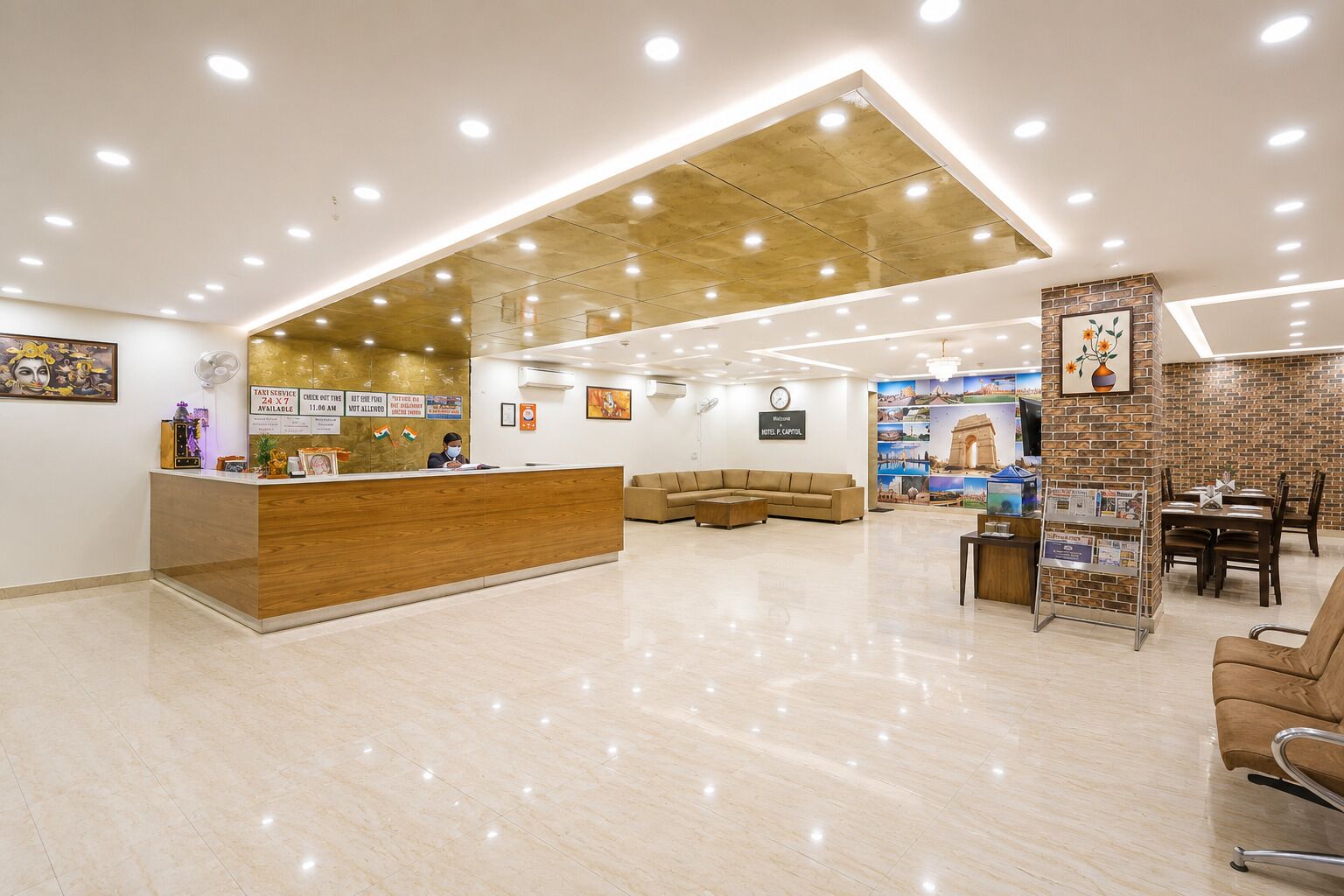 A hotel reception area with a wooden reception desk, a seating area with sofas, and a wall decorated with travel-themed artwork.