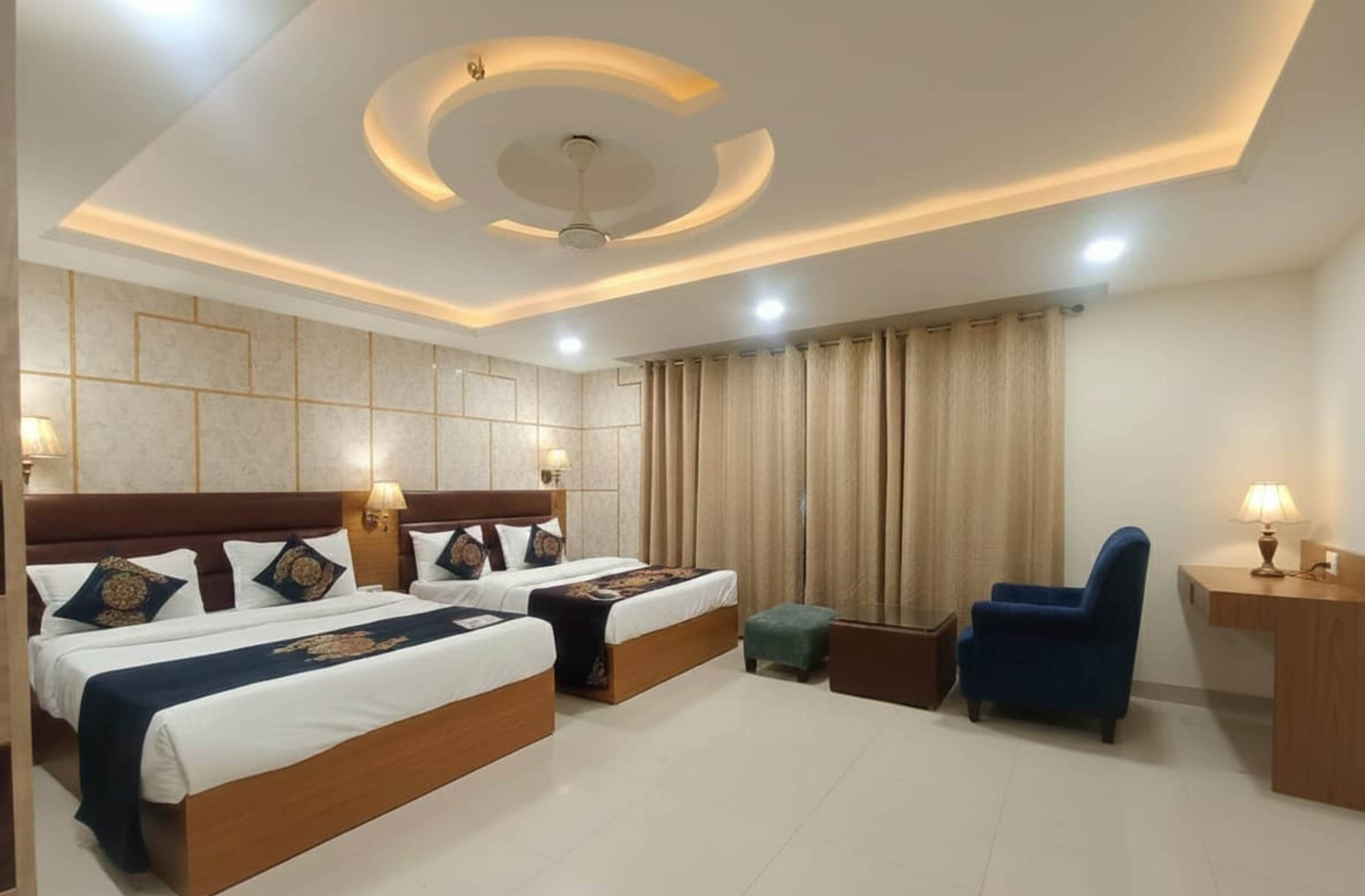 A hotel room with two beds, a desk, a chair, and a ceiling fan.