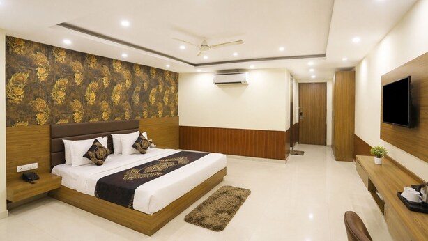 A modern hotel room with a large bed, a flat-screen TV, a desk, and a ceiling fan. - Hotel D'Capitol- Delhi Airport (New Delhi)