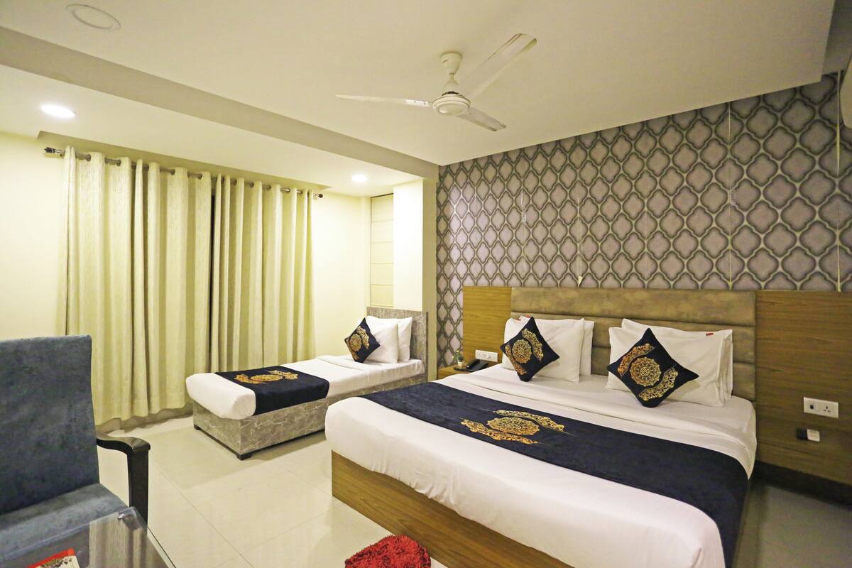 A hotel room with two single beds, a large bed, a ceiling fan, and a patterned wall.