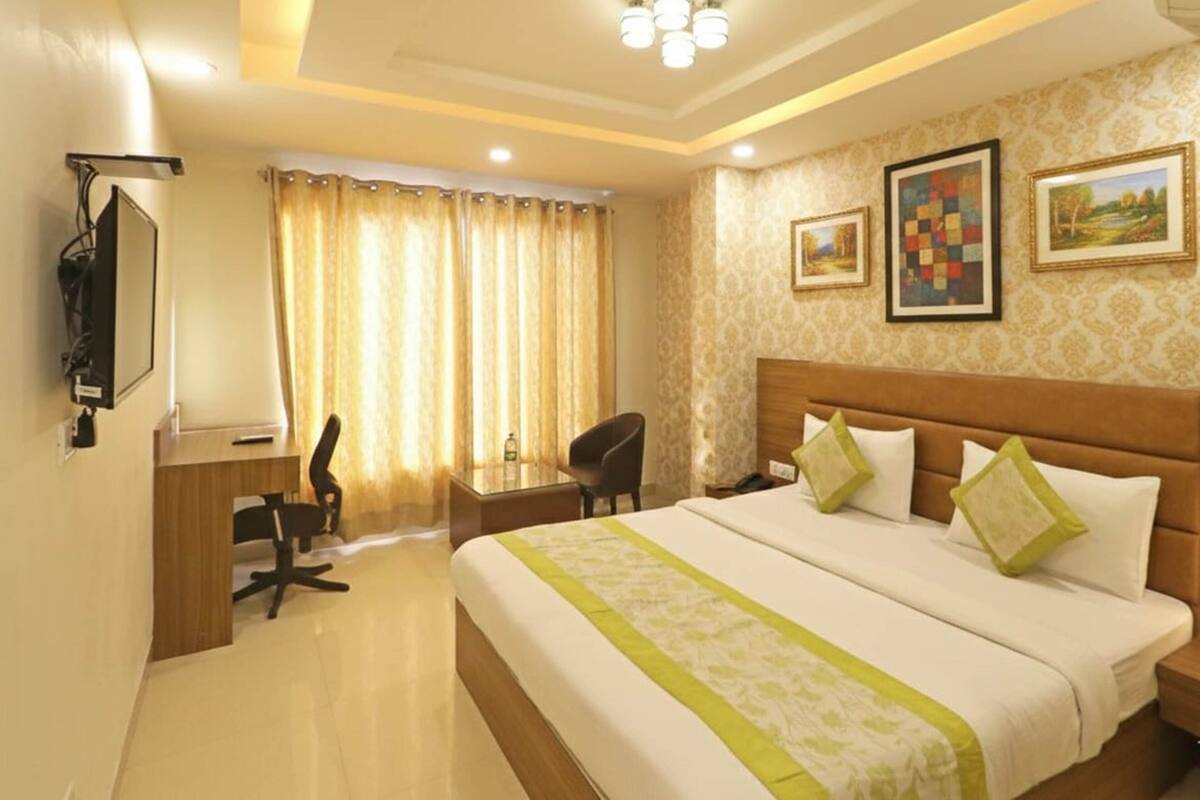 A hotel room with a large bed, a desk with a chair, a television, and two framed pictures on the wall.