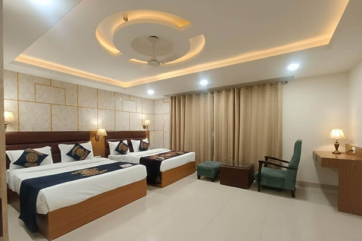 A hotel room with two beds, a desk, a chair, and a ceiling fan.