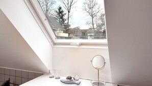 Een dakraam in een badkamer met een spiegel en twee glazen op een wit aanrecht.