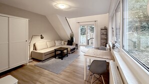 Een moderne, goed verlichte woonkamer met een bank, salontafel en een eethoek met een stoel en tafel. Een groot raam biedt uitzicht op de omgeving.