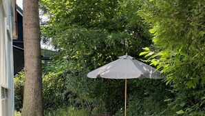 Een terras buiten met een tafel en stoelen, een gestreepte parasol en een lantaarn.