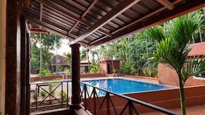 A covered pool area with a red carpet, metal railing, and a view of a swimming pool and greenery. - Aashrayam Hotels And Resorts (Honavar)