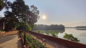 A park with a paved walkway, benches, and a view of a calm lake. - Aashrayam Hotels And Resorts (Honavar)