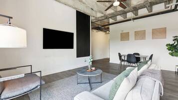 Ein modernes Wohnzimmer mit grauem Sofa, einem runden Couchtisch und einem Essbereich mit Tisch und Stühlen.