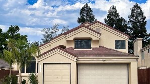 A two-story house with a beige exterior, a red-tiled roof, and a garage.